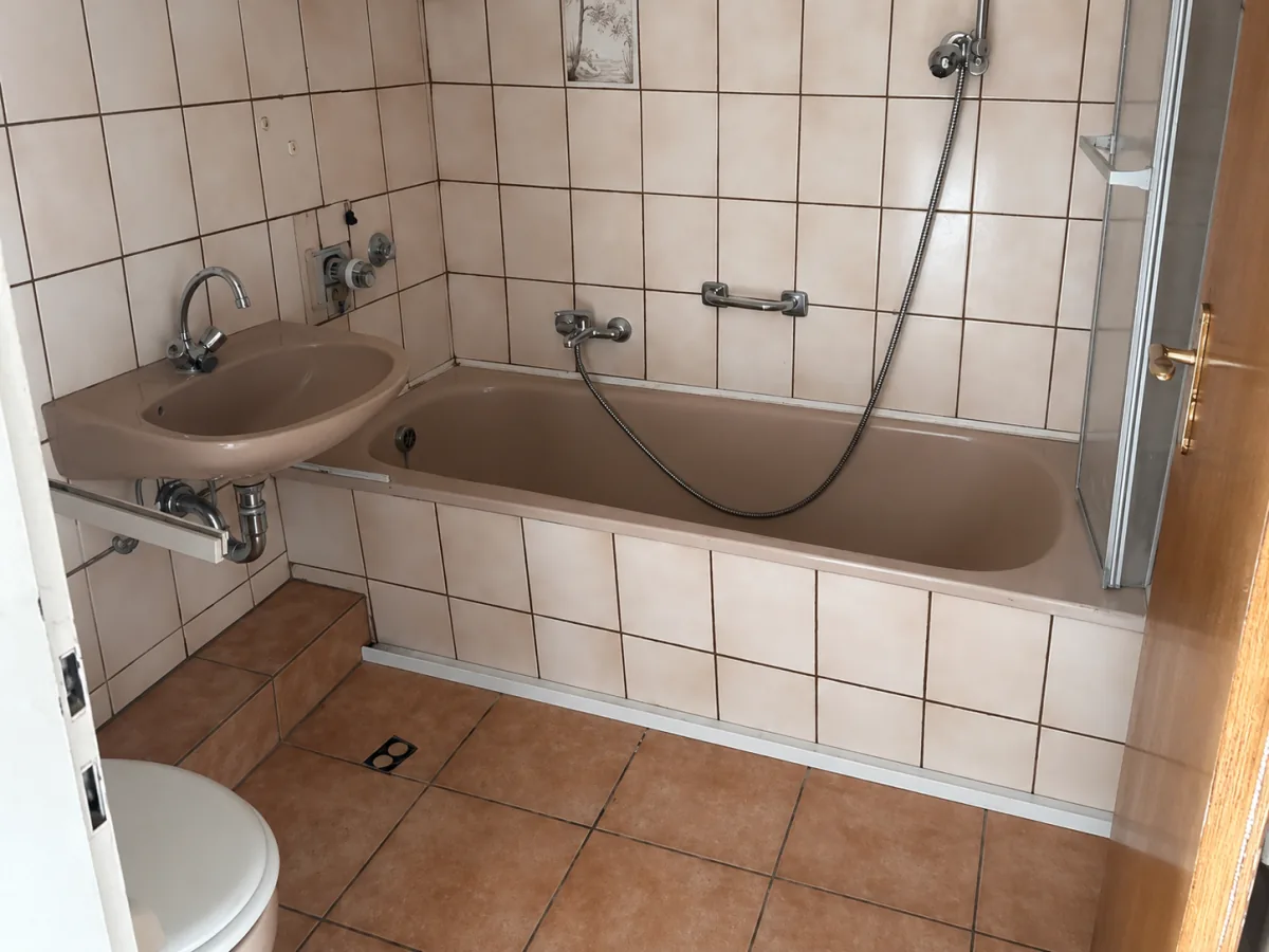 Echtes Referenzfoto eines Badezimmers vor Sanierung mit alten Fliesen und Badewanne