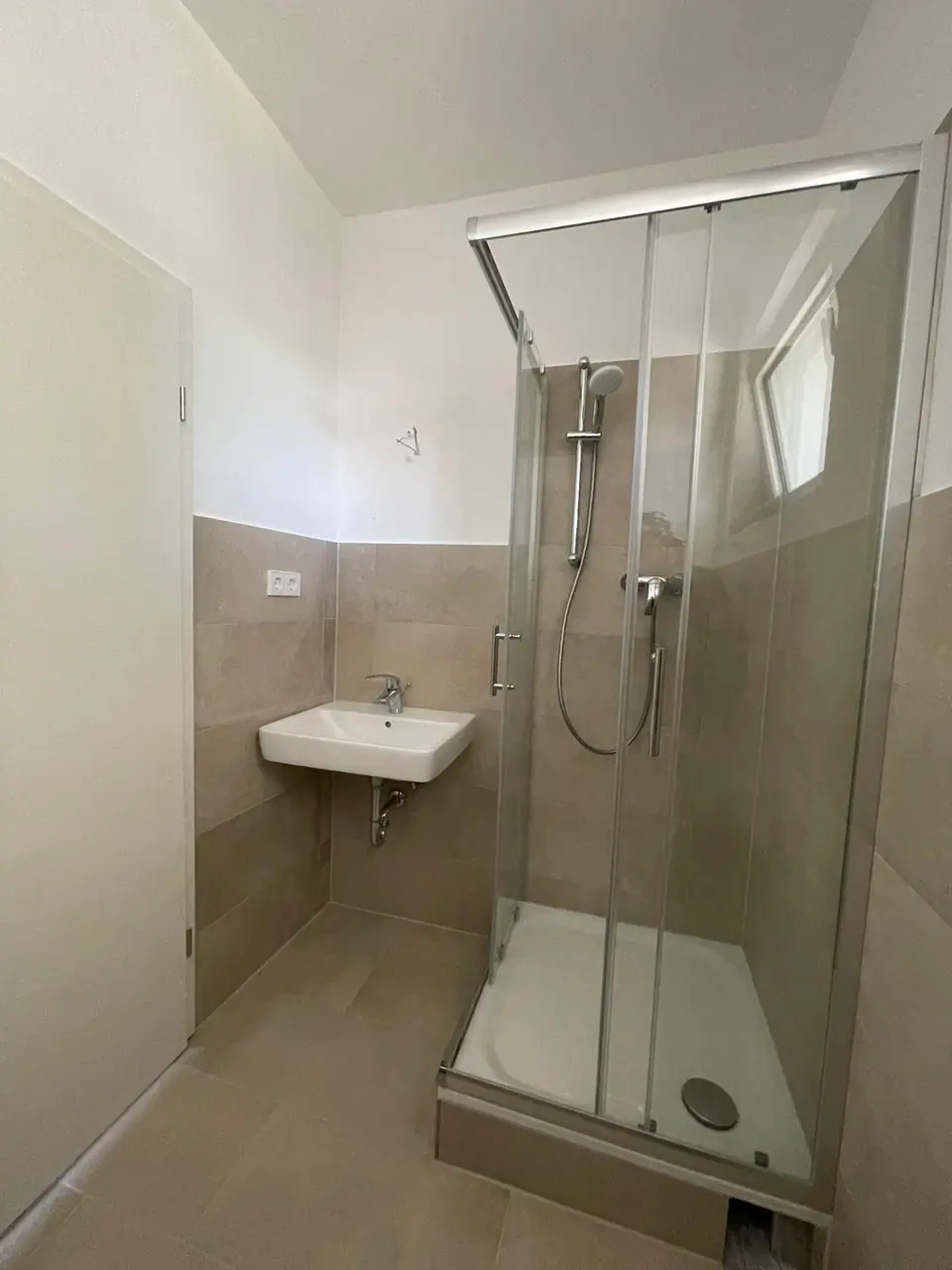 Echtes Referenzfoto eines fertiggestellten Duschbads mit Glasdusche, Waschbecken und beigen Wandfliesen