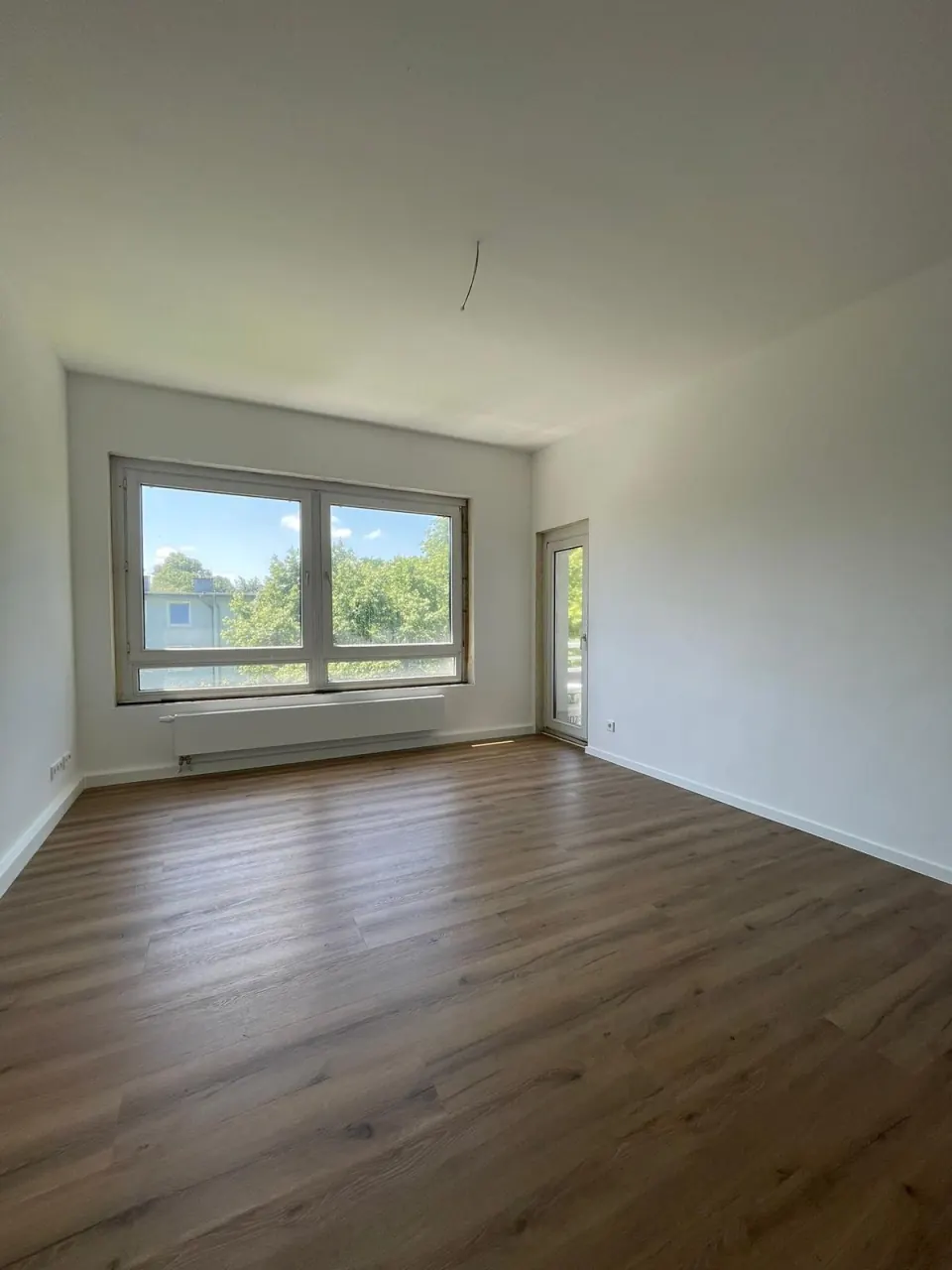Echtes Referenzfoto: heller Wohnraum nach der Renovierung mit neuem Laminatboden und großer Fensterfront