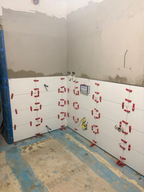 Badezimmer während der ersten Fliesenreihen mit weißen Wandfliesen und Distanzhaltern