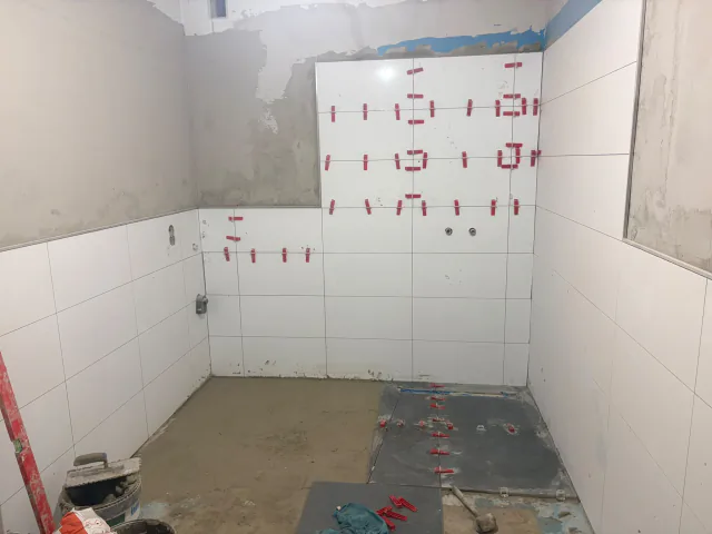 Badezimmer mit weitgehend verlegten weißen Wandfliesen und grauer Bodenfläche im Baustand