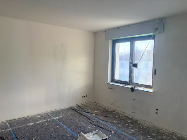 Zimmer mit fertigen hellen Wandflächen, Fenster und noch geschütztem Boden