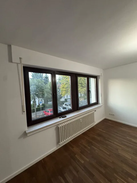 Renovierter Wohnraum mit großer Fensterfront, Heizkörpern, weißen Wänden und dunklem Boden in Holzoptik