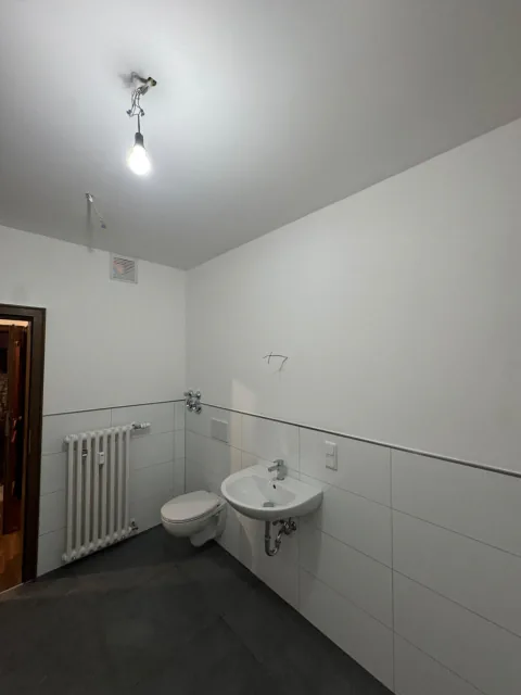 Helles Badezimmer mit weißen Wandfliesen, grauem Boden, Waschbecken und Wand-WC