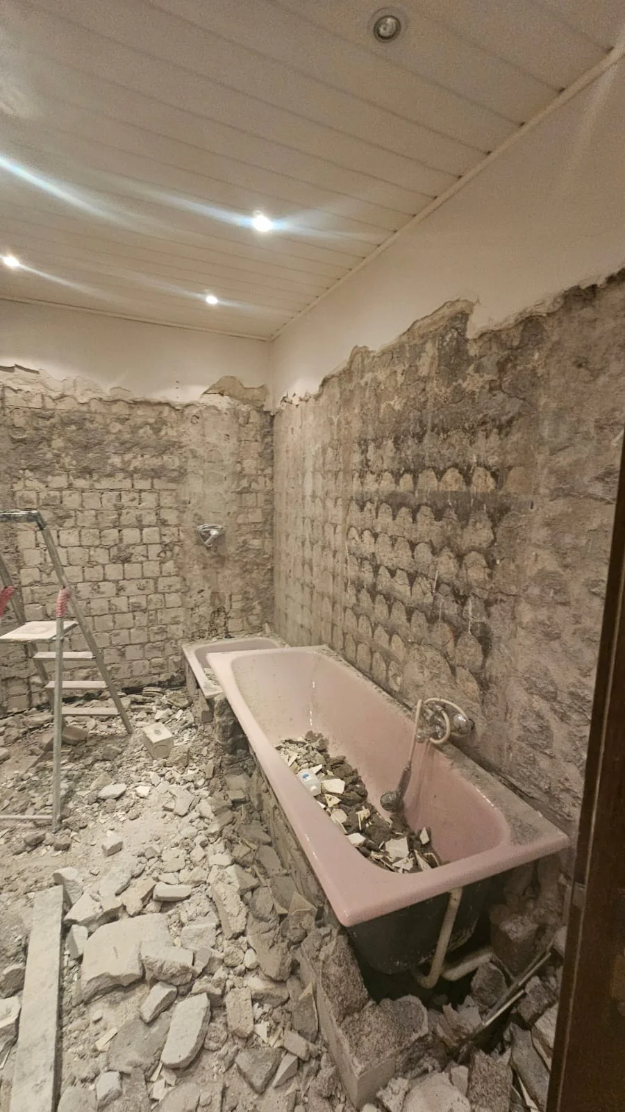 Badezimmer im Rückbau mit alter Badewanne, freigelegtem Mauerwerk und Bauschutt