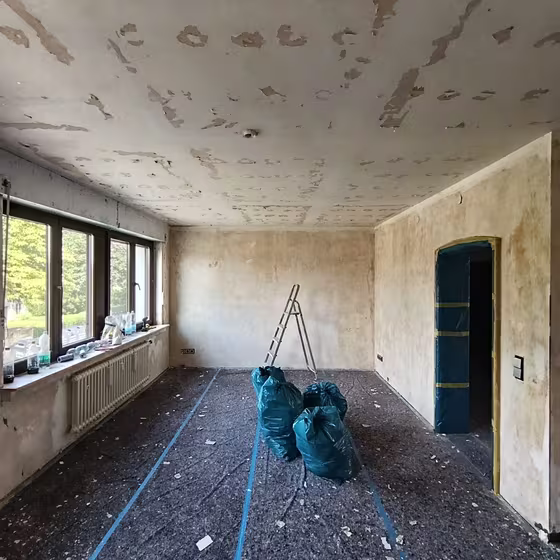 Großer Wohnraum nach der Entkernung mit Fensterfront, offenem Boden und bearbeiteter Decke