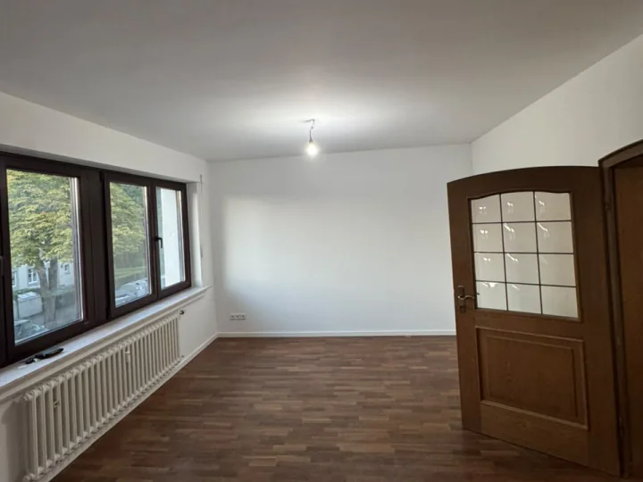 Renovierter großer Wohnraum mit weißen Wänden, dunklem Boden in Holzoptik und Fensterfront